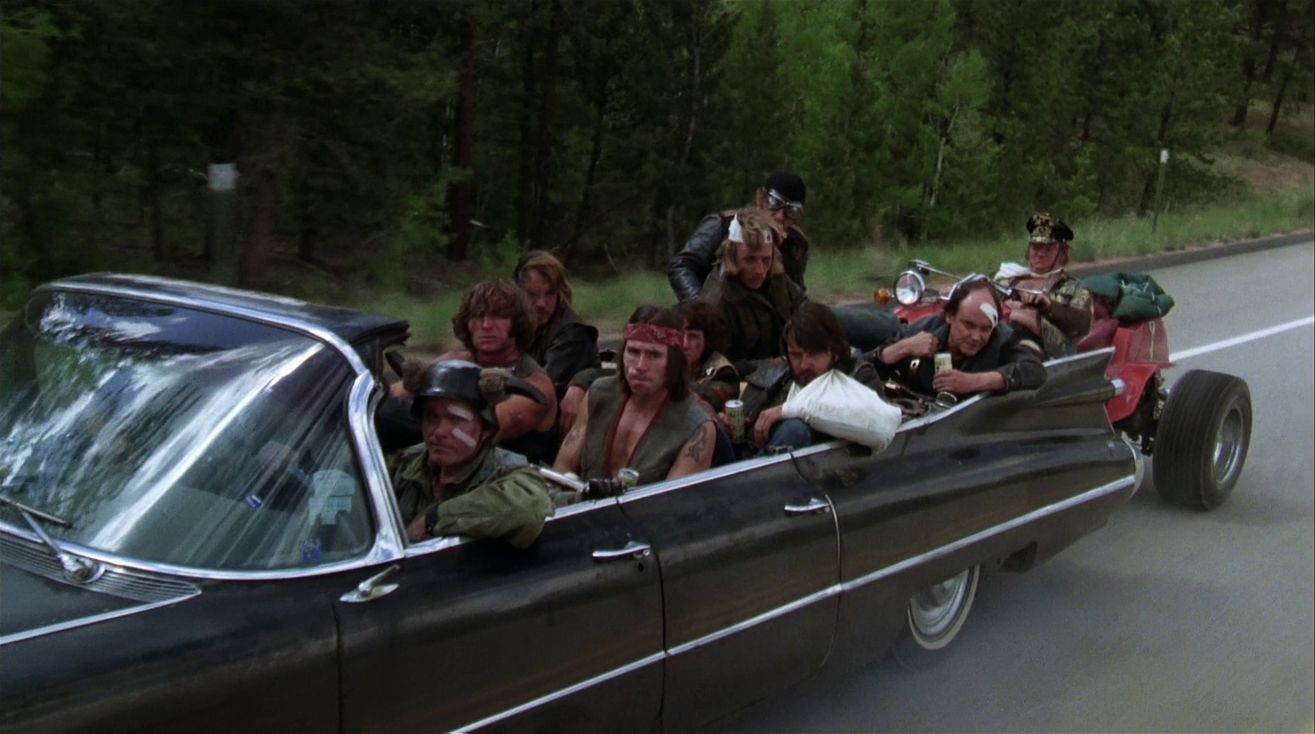 HD PC wallpaper of a packed convertible with passengers and an orangutan on the roof, roaring down a forest road — scene from the movie Every Which Way But Loose.