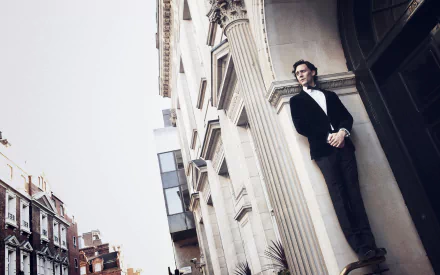 A stylish Tom Hiddleston stands beside a grand building, wearing a tuxedo. This high-definition image serves as a striking desktop wallpaper for fans and admirers.