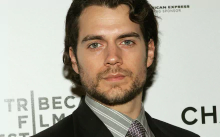 A close-up of British actor Henry Cavill, showcasing his strong features and charismatic presence, set against a branded backdrop at an event. A stylish HD desktop wallpaper.