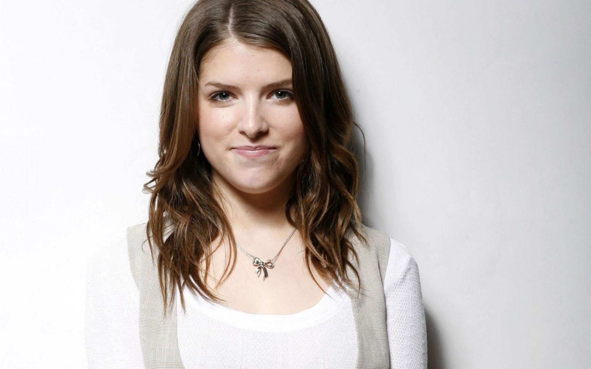 HD desktop wallpaper featuring American actress and celebrity Anna Kendrick against a plain light background, smiling softly with loose wavy hair.
