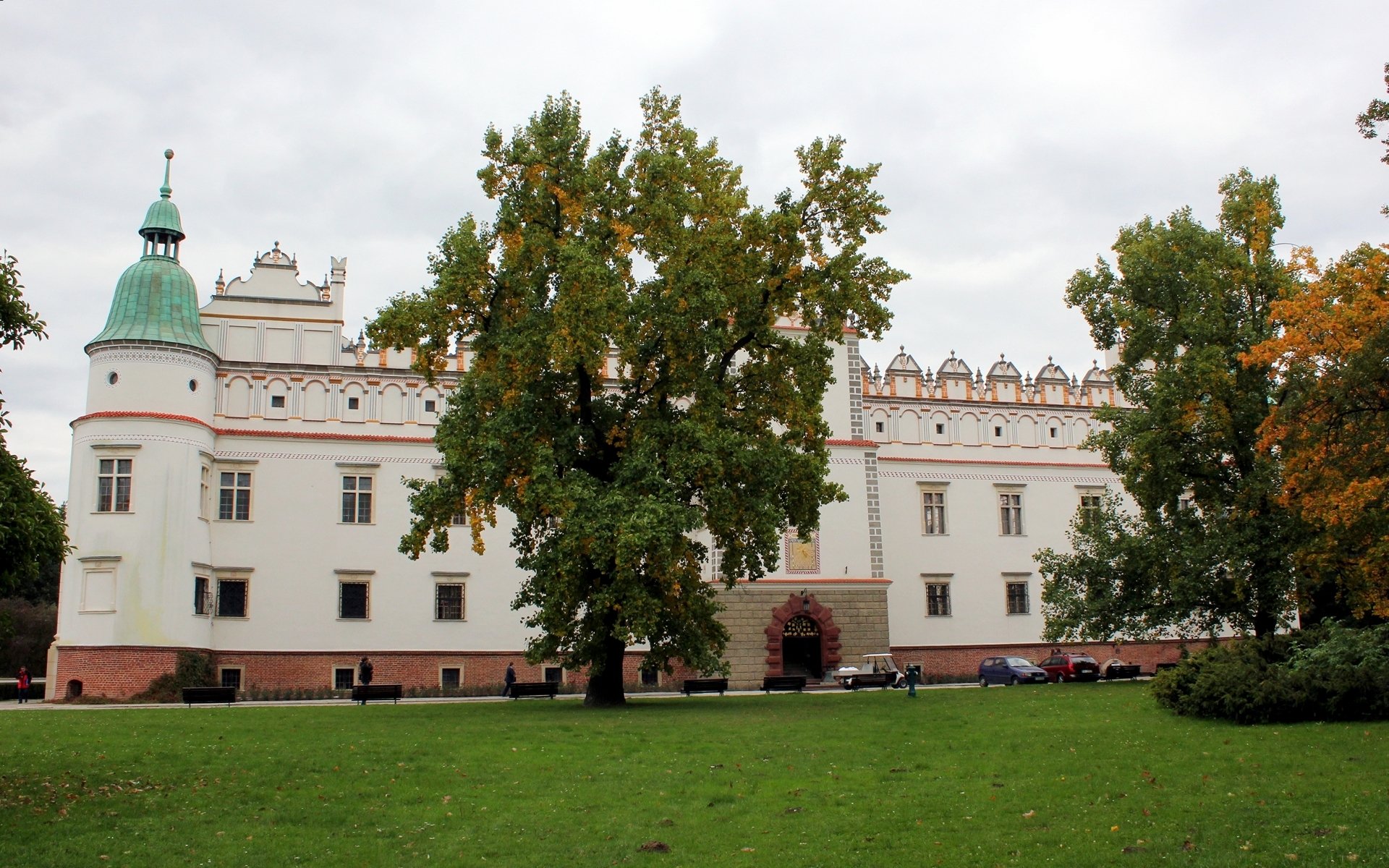 HD desktop wallpaper featuring the Baranów Sandomierski Castle, a historic man-made structure surrounded by greenery under a cloudy sky.