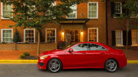 HD desktop wallpaper featuring a sleek red Mercedes-Benz CLA-Class parked in front of a brick townhouse at dusk.