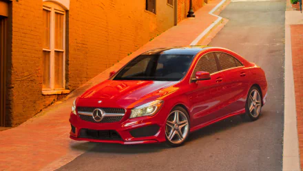 HD PC desktop wallpaper of a red Mercedes-Benz CLA-Class parked on a sunlit narrow street beside warm orange brick walls.