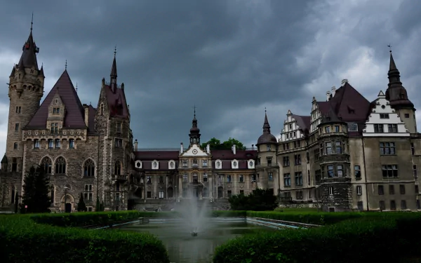 Moszna Castle under brooding clouds, fountain and formal gardens in foreground — HD PC desktop wallpaper