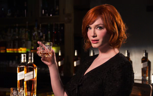 HD desktop wallpaper featuring American actress Christina Hendricks holding a glass in a dimly lit bar setting.
