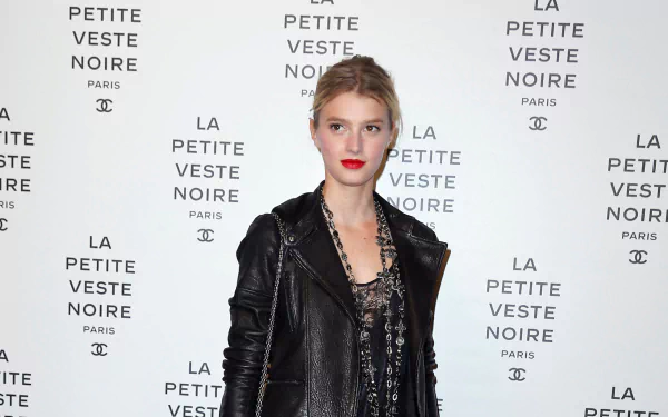 French model Sigrid Agren poses confidently against a branded backdrop, wearing a black leather jacket and stylish ensemble in this HD desktop wallpaper.