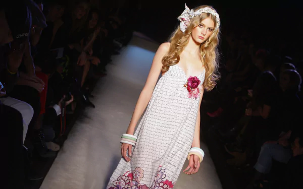 HD desktop wallpaper featuring French model Sigrid Agren walking the runway in a white dress adorned with pink floral details.