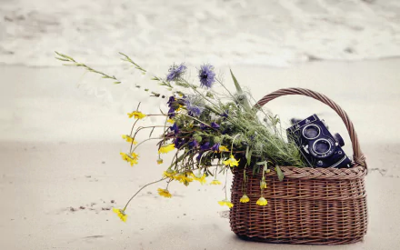HD desktop wallpaper featuring a wicker basket on the beach, filled with wildflowers and a vintage man-made camera.