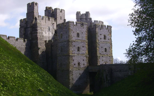 HD PC desktop wallpaper of man-made Arundel Castle: weathered stone keep rising above a grassy moat under a pale blue sky.
