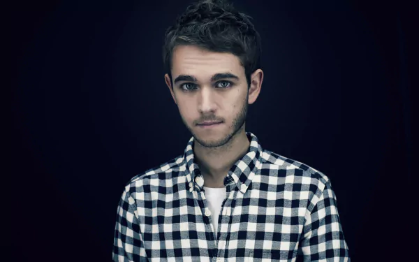 Studio portrait of a young man in a checked shirt, moody lighting suggesting electronic music energy against a dark backdrop — 5K Ultra HD PC desktop wallpaper.