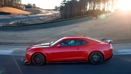 HD PC desktop wallpaper featuring a red Chevrolet Camaro Z28 driving on a sunlit race track surrounded by trees.