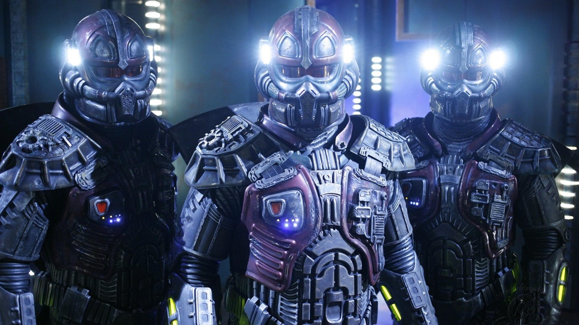 Three armored Jaffa warriors from the TV show Stargate SG-1 with glowing helmets and chest lights, shown as a 2K Quad HD PC desktop wallpaper/background.