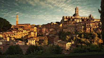 HD PC desktop wallpaper of Siena's man-made skyline: sunlit medieval rooftops, cathedral and Torre del Mangia rising over terraced hillside under a dramatic sky.
