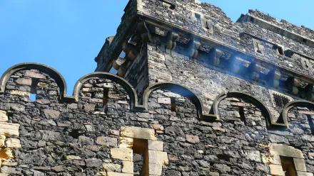 Close-up of Grodziec Castle's weathered stone battlements and crenellated tower against a clear blue sky — 2K Quad HD man-made architectural desktop wallpaper.