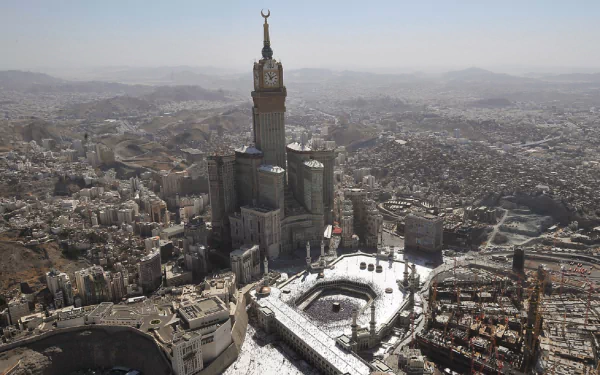 An aerial view of the Mecca Clock Tower, showcasing its impressive architecture against the sprawling landscape of Mecca. A stunning HD desktop wallpaper and background.
