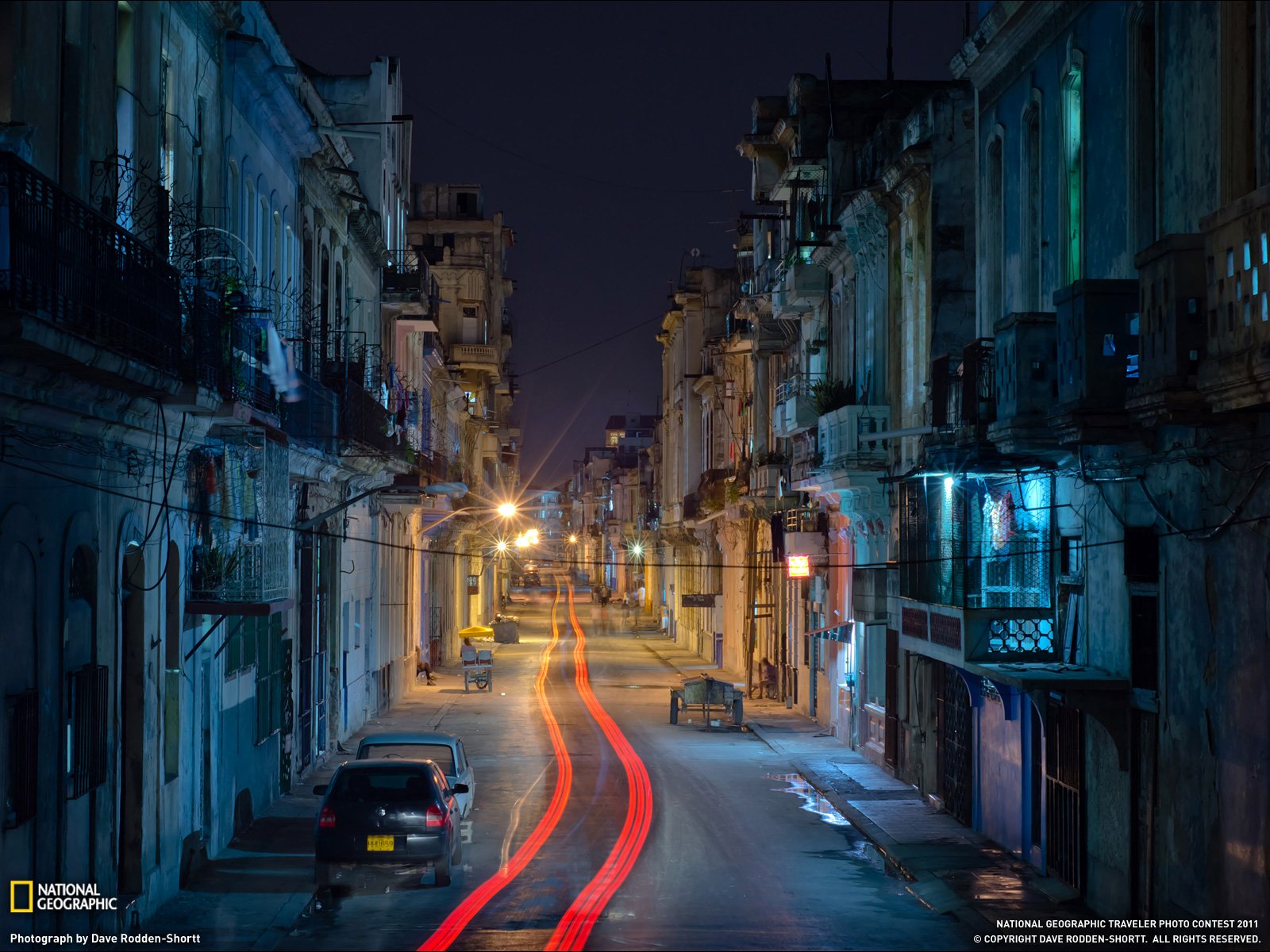 Man-made urban scene in Havana at night: narrow colonial street with balconies, parked cars and red light trails — HD PC desktop wallpaper/background.