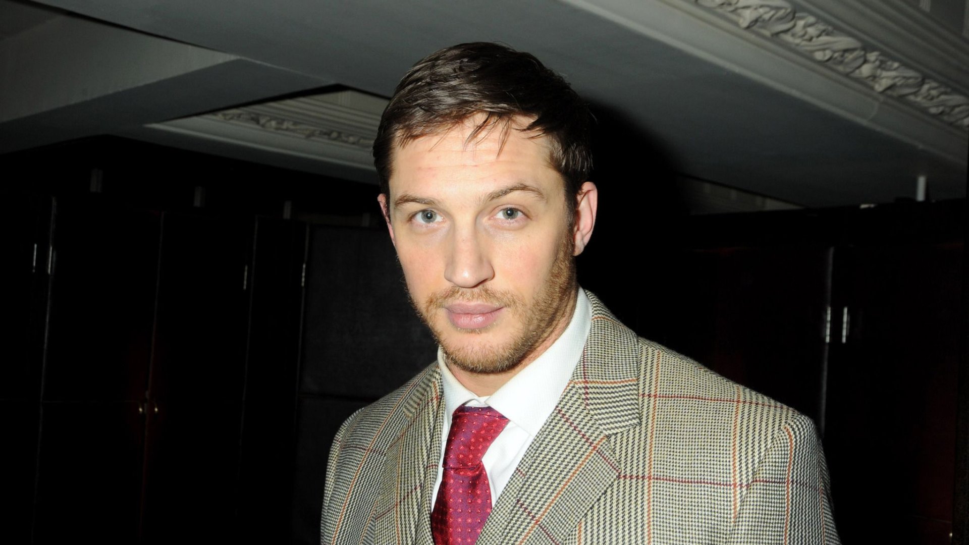 Portrait of English actor and celebrity Tom Hardy in a checked suit and red tie, featured as a 4K Ultra HD PC desktop wallpaper and background.