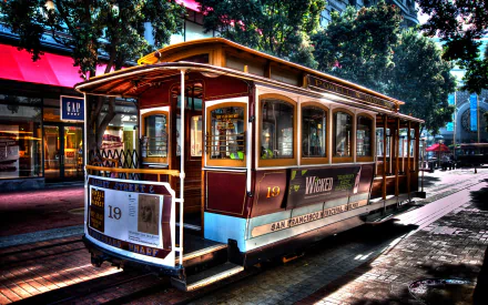 HD desktop wallpaper featuring a vintage red and brown tram on a sunlit urban street surrounded by trees and shops.