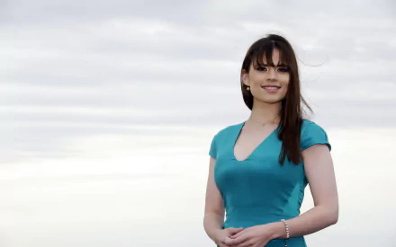 HD desktop wallpaper featuring English actress and celebrity Hayley Atwell smiling in a turquoise dress against a cloudy sky background.
