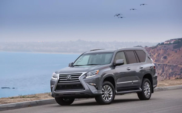 HD PC desktop wallpaper featuring a dark gray Lexus GX parked on a coastal road with cliffs and ocean in the background under a cloudy sky.