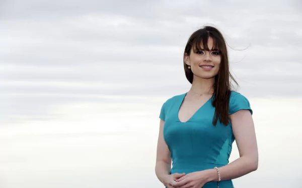 HD desktop wallpaper featuring English actress and celebrity Hayley Atwell smiling in a turquoise dress against a cloudy sky background.