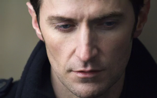 HD PC desktop wallpaper: close-up portrait of a contemplative English man in a dark coat, downcast gaze and soft-lit face.