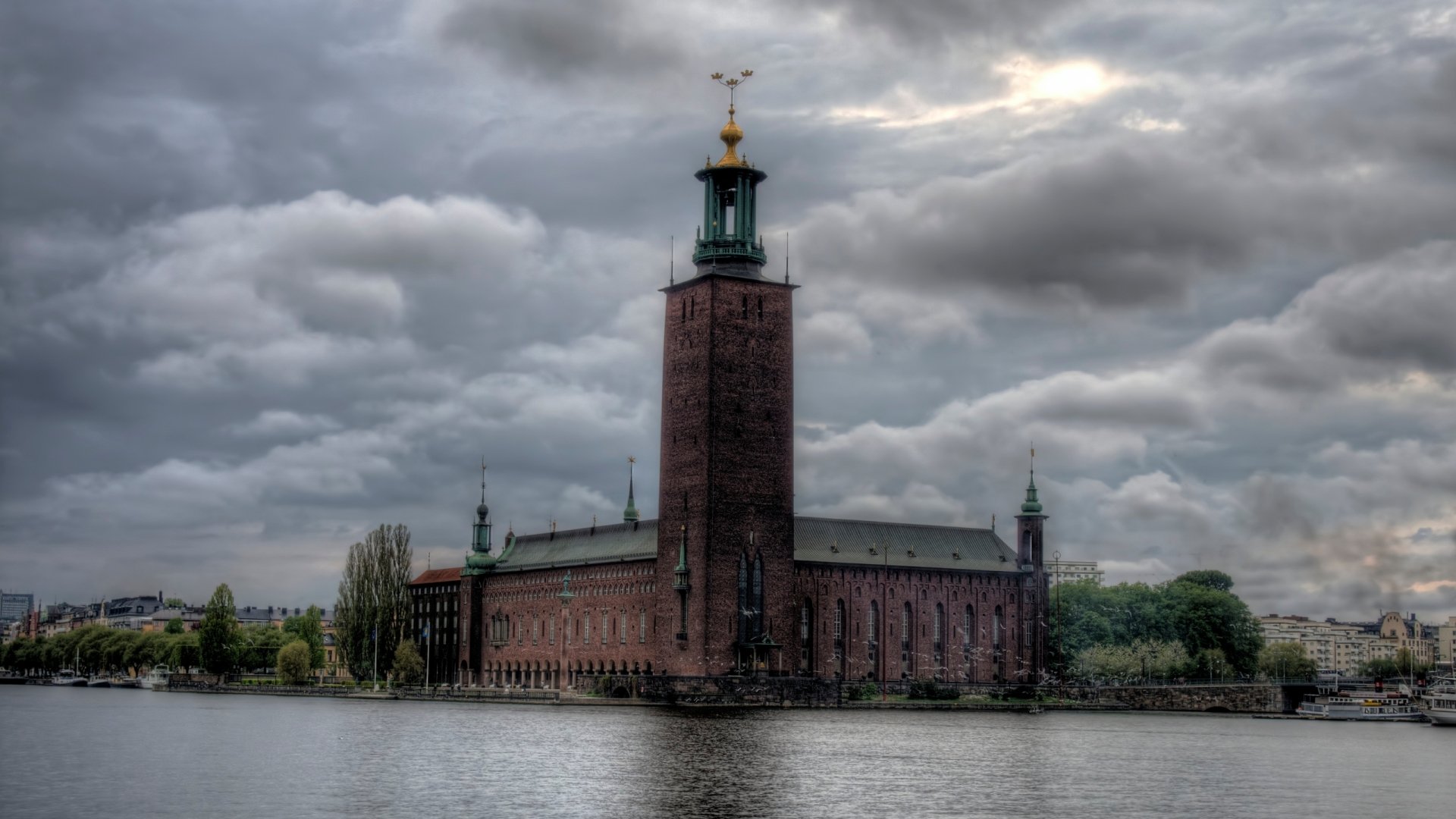 Moody view of Stockholm's brick City Hall tower by the water, Sweden — man-made architecture rendered as a 2K Quad HD PC desktop wallpaper background.