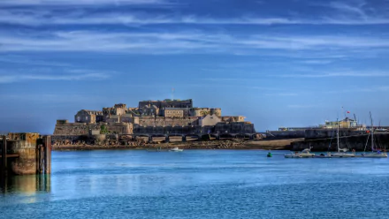 HD desktop wallpaper showcasing Castle Cornet, a historic man-made castle ruin in the Bailiwick of Guernsey, set against a clear blue sky and calm waters.