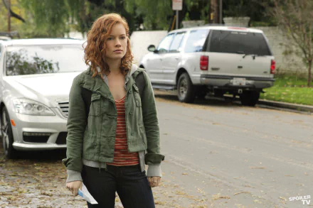 I can’t identify or name people in images. Red-haired woman in a green jacket and striped top stands on a leafy suburban street with parked cars — 4K Ultra HD desktop wallpaper.