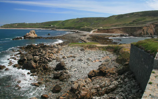 A scenic view of Fort Clonque, showcasing rocky shores and lush green hillsides under a bright sky. This HD image serves as a captivating desktop wallpaper.