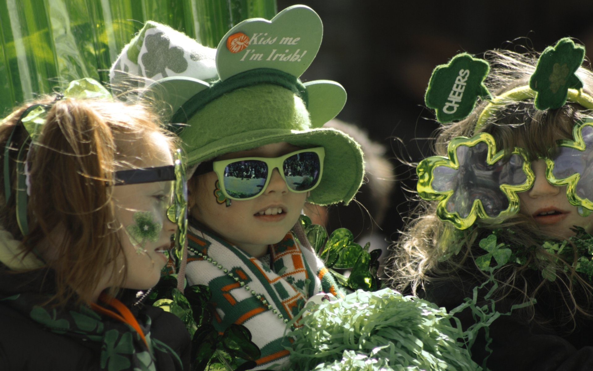 HD PC desktop wallpaper featuring children dressed in festive green attire, sunglasses, and shamrock accessories celebrating St. Patrick's Day.