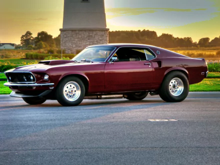 HD desktop wallpaper showcasing a classic Ford Mustang Fastback parked on a sunlit road with a stone monument and trees in the background.