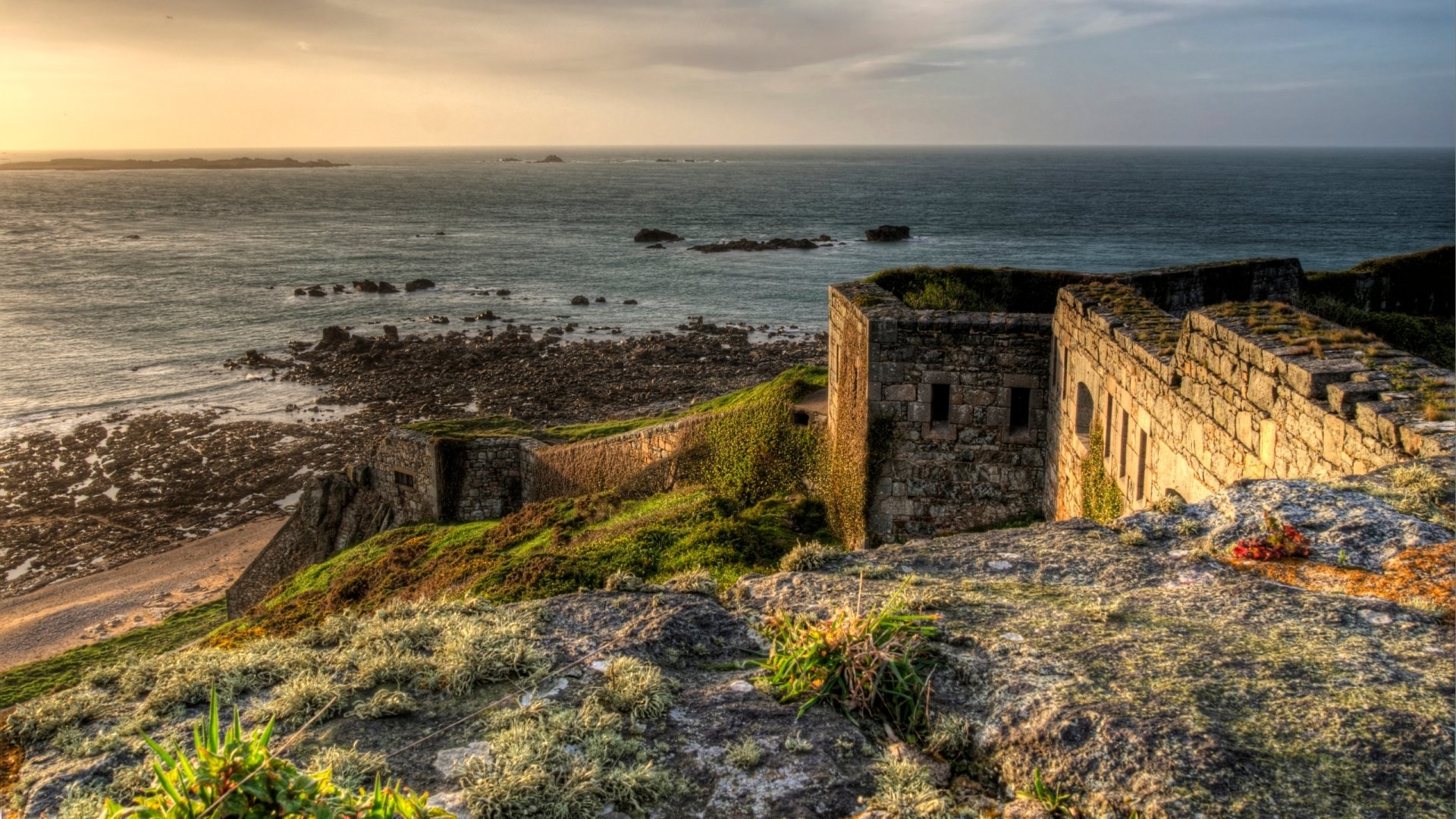 Man-made Fort Tourgis on rocky cliffs overlooking the sea at sunset, 2K Quad HD PC desktop wallpaper and background.