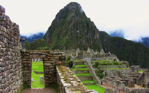 HD desktop wallpaper showing the man-made ancient stone ruins of Machu Picchu with lush green terraces and towering mountain backdrop under a cloudy sky.
