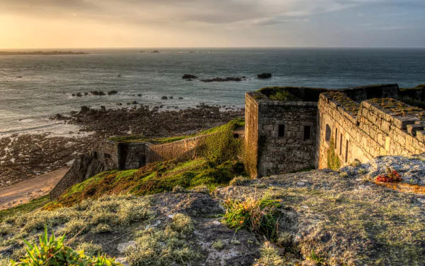 Man-made Fort Tourgis on rocky cliffs overlooking the sea at sunset, 2K Quad HD PC desktop wallpaper and background.