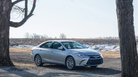 Silver 2015 Toyota Camry vehicle parked on gravel between trees with snowy fields and a pale sky — HD PC desktop wallpaper/background.