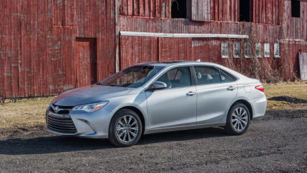 Silver 2015 Toyota Camry parked on a gravel driveway in front of a weathered red barn, captured in a high-definition desktop wallpaper image.
