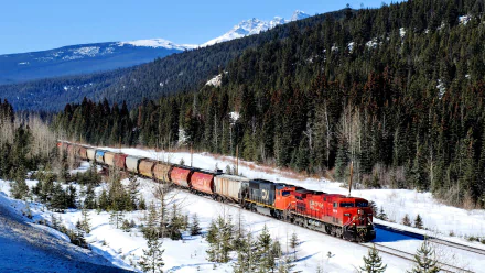 A vibrant red train travels through a snowy forested landscape with mountains in the background, captured in an HD PC desktop wallpaper and background.