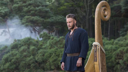 Ragnar Lothbrok from Vikings (2013) stands beside a Viking ship amidst a forest backdrop in this 4K Ultra HD PC desktop wallpaper and background.