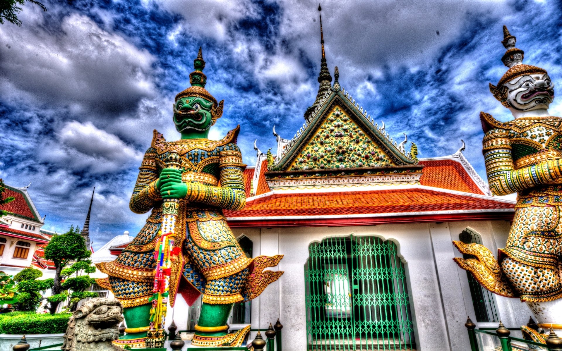 HD PC desktop wallpaper featuring the ornate guardian statues and intricate architecture of the religious Wat Arun Temple under a dramatic cloudy sky.