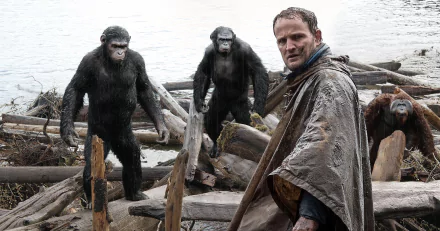 HD PC desktop wallpaper from the movie Dawn of the Planet of the Apes: a weathered man in a cloak stands on a wrecked shoreline as two apes approach behind him.