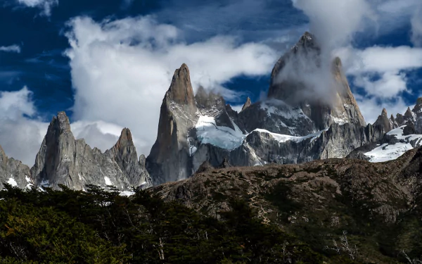 Nature HD PC desktop wallpaper/background: Mount Fitz Roy's jagged, snow-capped peaks piercing clouds above dark forest under a dramatic blue sky.