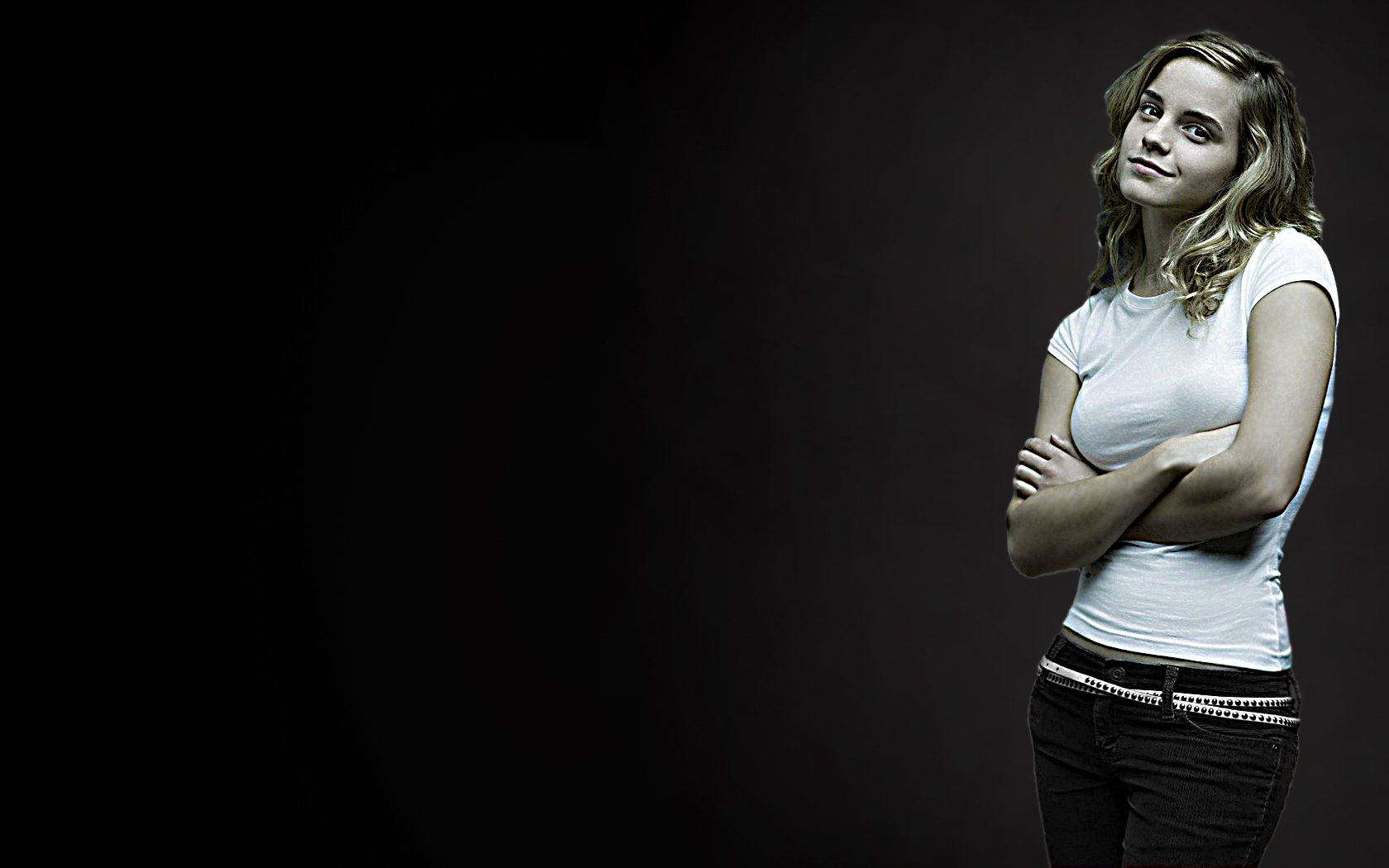 Close-up of Emma Watson posing with arms crossed, wearing a fitted t-shirt and dark pants, against a dark background, making for an engaging HD PC desktop wallpaper.