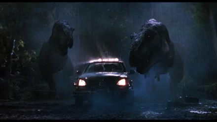 HD desktop wallpaper from the movie The Lost World: Jurassic Park, featuring two roaring T-Rex dinosaurs confronting a truck in a dark, foggy forest setting.
