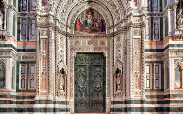 Religious HD desktop wallpaper of the Basilica of Saint Mary of the Flower's ornate marble facade and carved bronze doors, with decorative arches and colorful inlaid patterns.