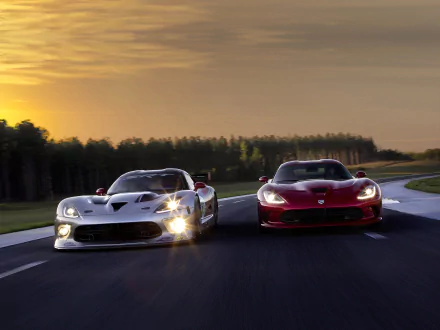Two Dodge Viper GTS-R race cars, one white and one red, speed side by side on a track at sunset in this HD PC desktop wallpaper.