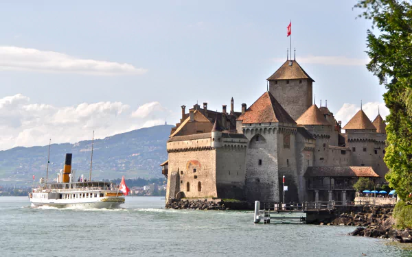 HD desktop wallpaper of the man-made Château de Chillon in Veytaux, Switzerland: medieval lakeside castle on Lake Geneva with a steamboat and distant mountains.