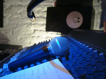 A close-up view of a microphone on a sound mixer, with a music note sheet nearby, set against a textured wall and speakers, creating a vibrant music-themed HD desktop wallpaper.
