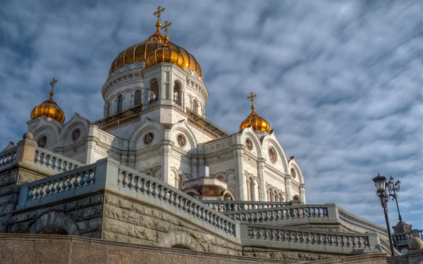 HD desktop wallpaper featuring the Cathedral of Christ the Saviour with golden domes under a textured cloudy sky, showcasing its religious and architectural grandeur.