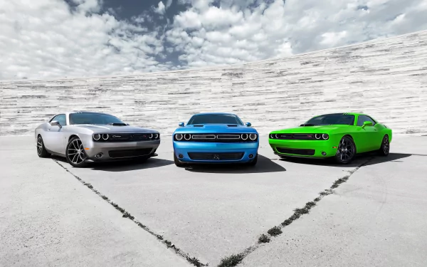 Three Dodge Challenger muscle cars (silver, blue, green) in a curved concrete arena under a cloudy sky — 2K Quad HD PC Desktop Wallpaper and Background, vehicle-focused composition.